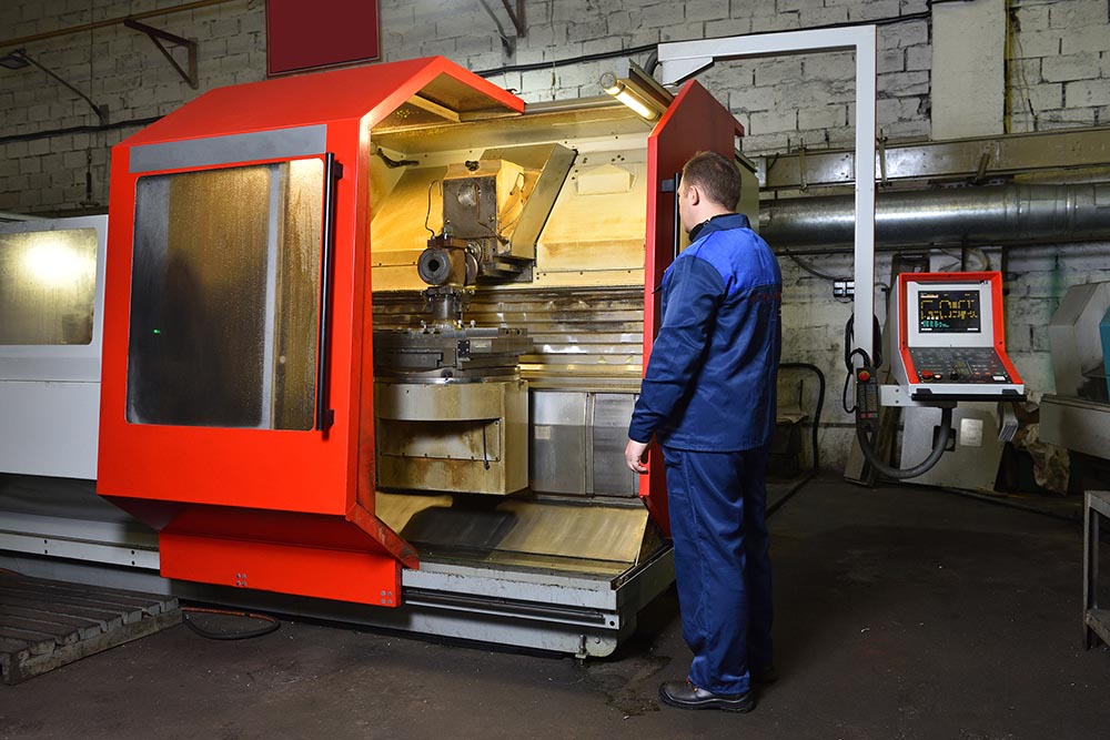 The worker in blue workwear, the operator of the CNC machine, oversees the process and controls it.